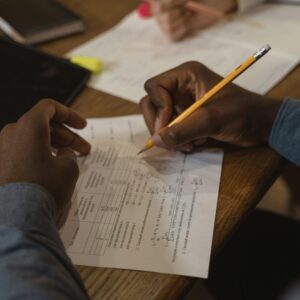 Close-up of a student writing on a test paper, focusing on solving problems with a pencil on a wooden desk.