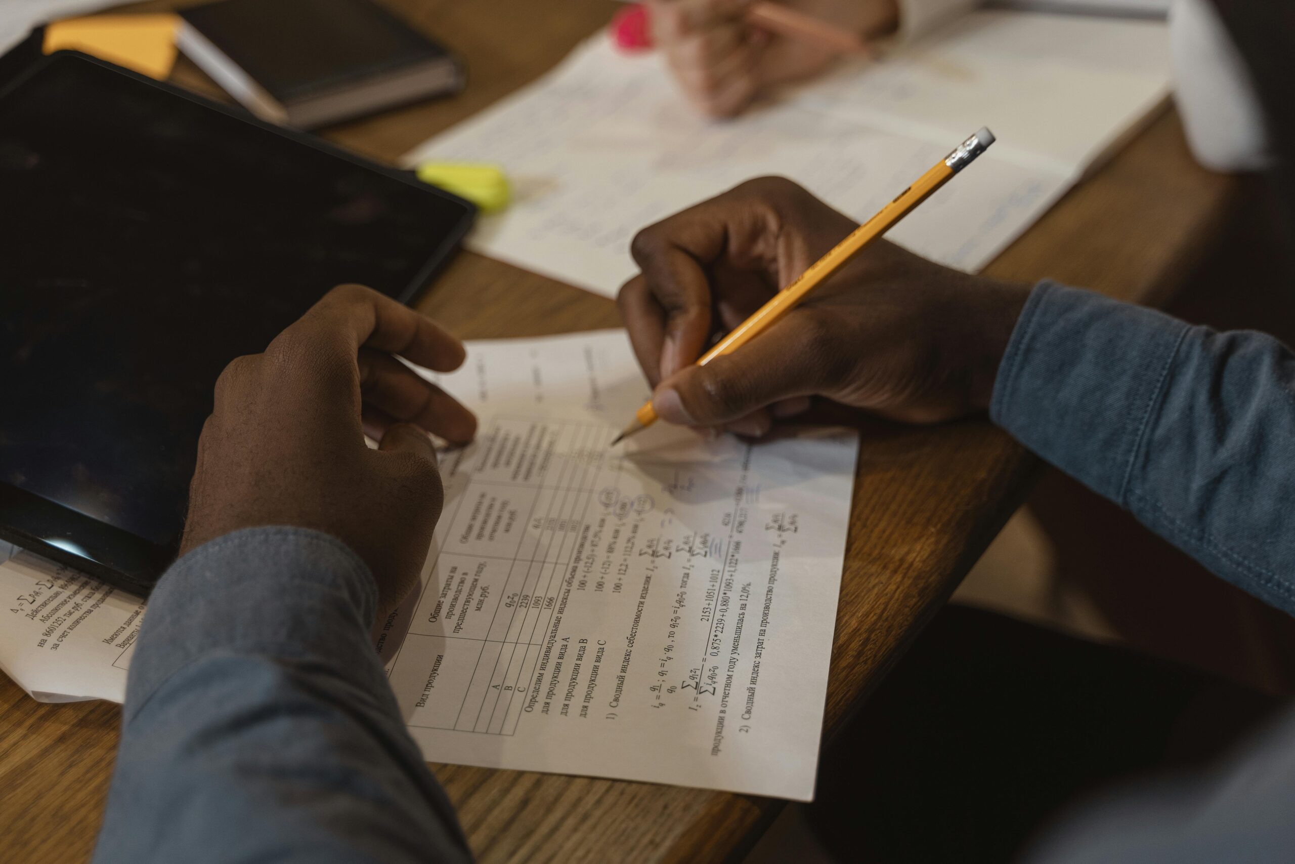 Close-up of a student writing on a test paper, focusing on solving problems with a pencil on a wooden desk.