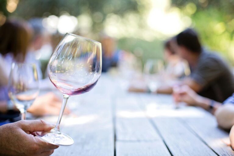 Wine glass with red wine on a wooden table at an outdoor gathering with blurred people.