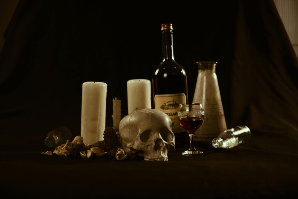 Dark still life with a skull, candles, and wine, evoking a mysterious atmosphere.