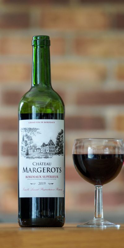 Close-up of Chateau Margerots Bordeaux wine bottle with a glass on a wooden surface.
