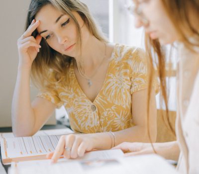 Two women collaborating on study materials in a bright library setting.