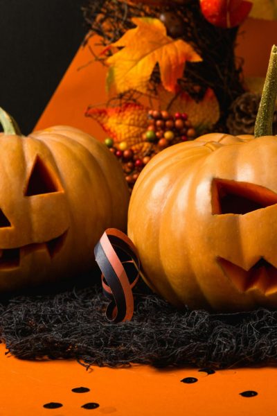 Two carved pumpkins with spooky faces set against an autumnal background for Halloween.