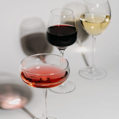 Three wine glasses with red, white, and rosé wines casting shadows on a white background.