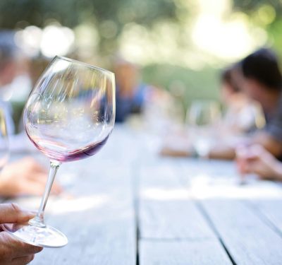 Wine glass with red wine on a wooden table at an outdoor gathering with blurred people.